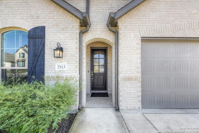 entrance to property featuring a garage and brick siding