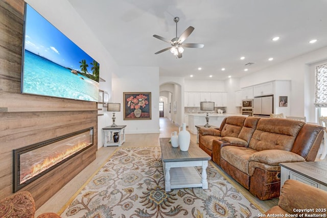living room with recessed lighting, arched walkways, a glass covered fireplace, and ceiling fan