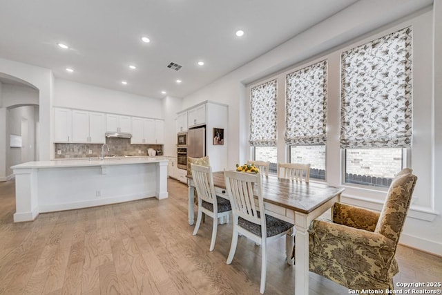 dining room with arched walkways, a healthy amount of sunlight, light wood finished floors, and recessed lighting