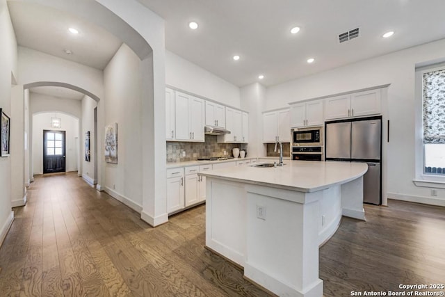 kitchen with a sink, under cabinet range hood, stainless steel appliances, visible vents, and arched walkways