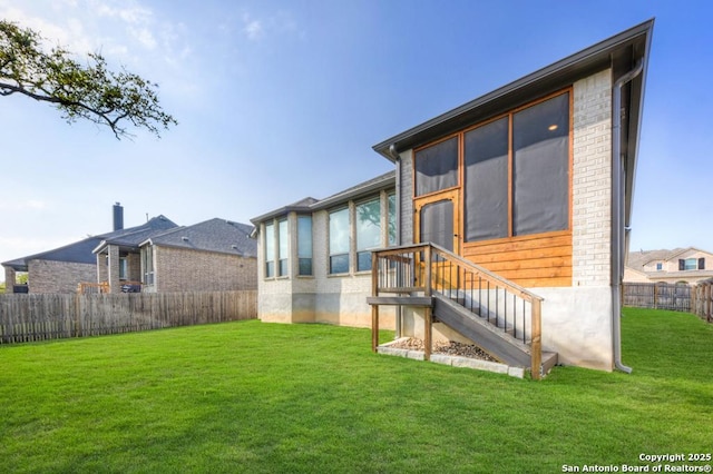 rear view of house with a lawn, a sunroom, and fence