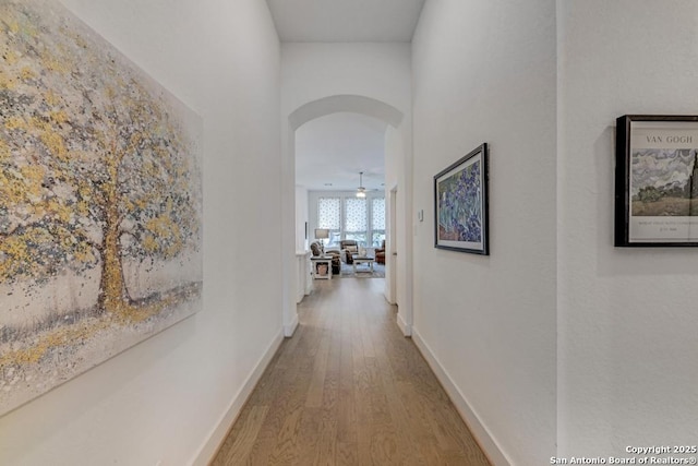 hall with baseboards, wood finished floors, and arched walkways