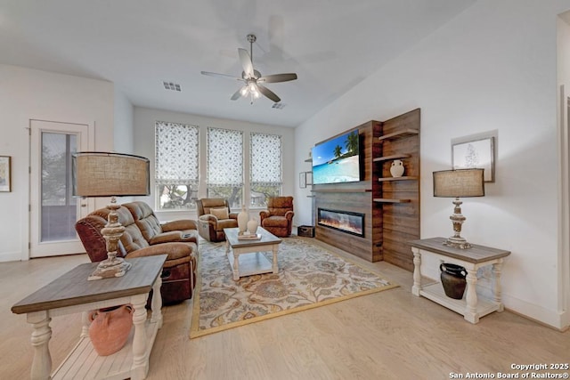 living room with wood finished floors, a glass covered fireplace, baseboards, visible vents, and ceiling fan