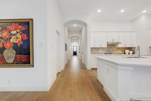 corridor featuring a sink, light wood-type flooring, baseboards, arched walkways, and recessed lighting