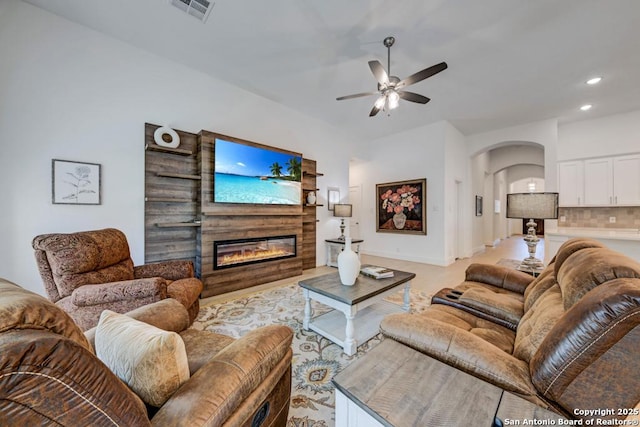 living room with visible vents, recessed lighting, a ceiling fan, arched walkways, and a glass covered fireplace