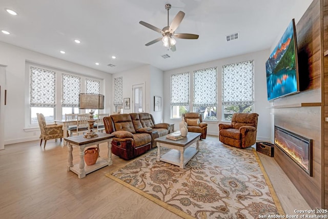 living area with ceiling fan, visible vents, a healthy amount of sunlight, and a glass covered fireplace