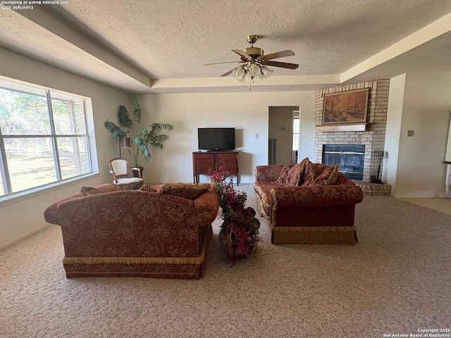 2501 Fischer Store, Wimberley, TX 78676 - carpeted living room featuring a textured ceiling, ceiling fan, a fireplace, a raised ceiling, and baseboards