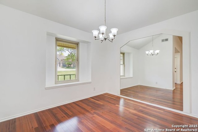 unfurnished dining area with lofted ceiling, baseboards, visible vents, a notable chandelier, and wood finished floors