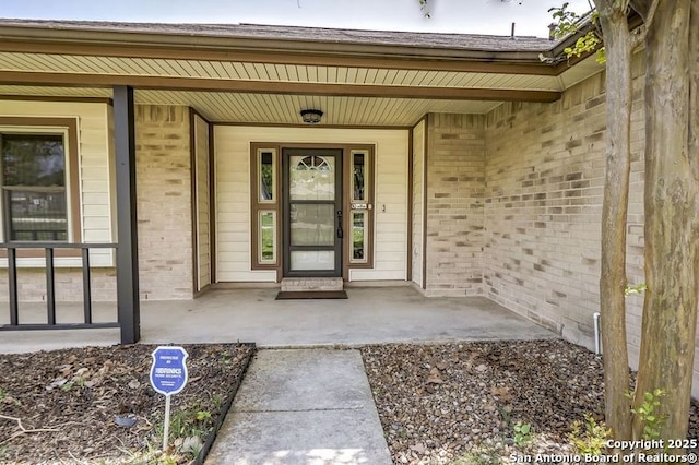 view of exterior entry with covered porch and brick siding