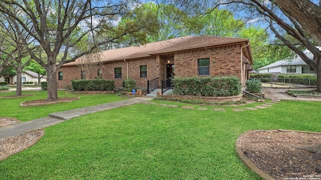 ranch-style home with brick siding, a shingled roof, fence, and a front lawn