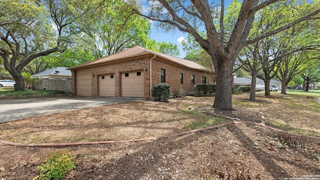 view of home's exterior featuring driveway, brick siding, a garage, and fence