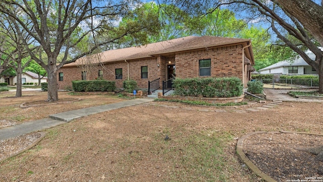 ranch-style home with fence, brick siding, and roof with shingles
