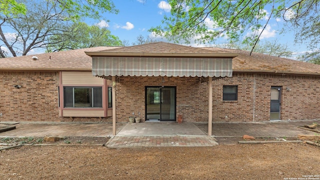 rear view of house featuring brick siding, a shingled roof, and a patio