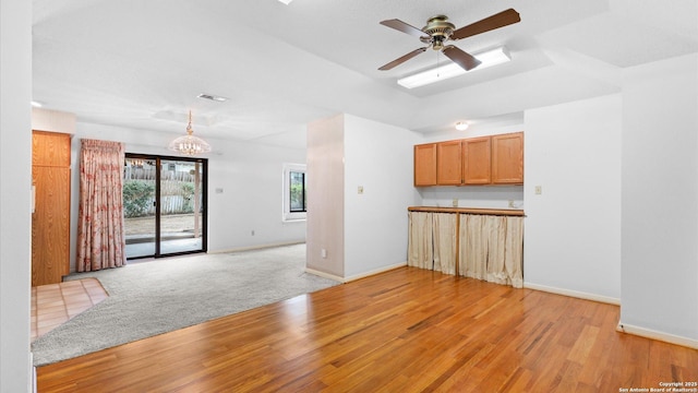 unfurnished living room featuring baseboards, visible vents, light wood-style floors, and ceiling fan with notable chandelier