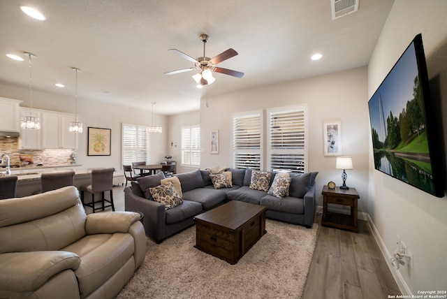 living room featuring baseboards, ceiling fan with notable chandelier, visible vents, light wood-style floors, and recessed lighting