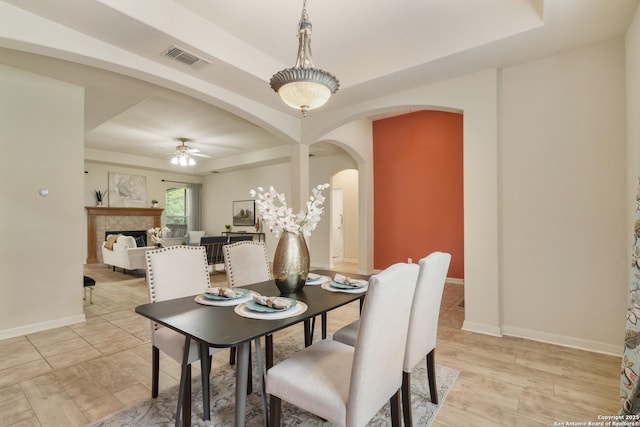 dining area featuring ceiling fan, a raised ceiling, a fireplace, arched walkways, and visible vents