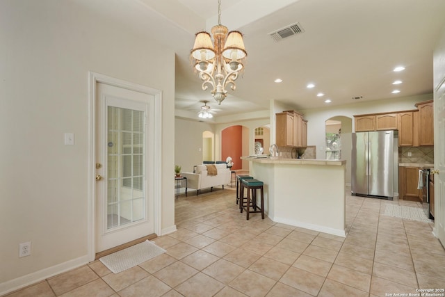 kitchen with arched walkways, freestanding refrigerator, open floor plan, decorative backsplash, and visible vents