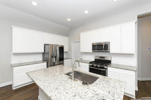 kitchen with white cabinets, appliances with stainless steel finishes, an island with sink, a sink, and backsplash