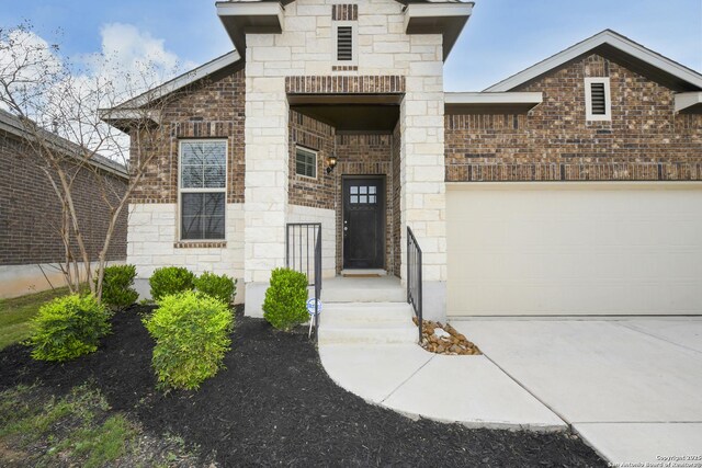 view of exterior entry with driveway, brick siding, a garage, and stone siding
