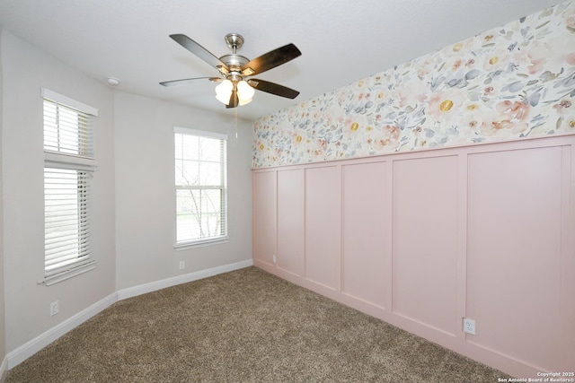 carpeted empty room with wallpapered walls, a ceiling fan, a decorative wall, and wainscoting