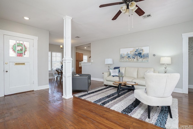 living area featuring baseboards, a ceiling fan, visible vents, ornate columns, and wood finished floors