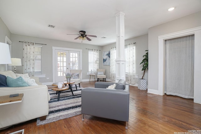 living room featuring decorative columns, a ceiling fan, visible vents, wood finished floors, and baseboards