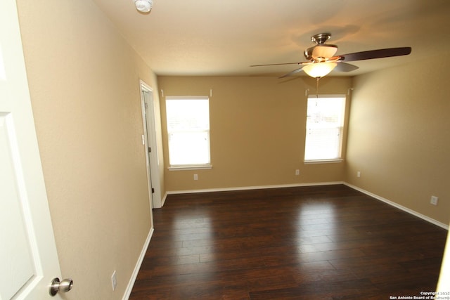 spare room featuring a healthy amount of sunlight, ceiling fan, baseboards, and dark wood-style floors