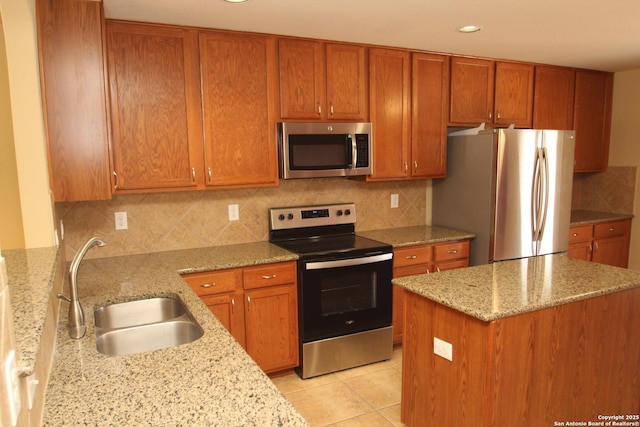 kitchen with light tile patterned floors, light stone countertops, brown cabinetry, stainless steel appliances, and a sink