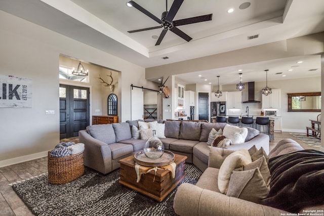 112 Chinkapin, Boerne, TX 78006 - living room featuring light wood-type flooring, a barn door, visible vents, a raised ceiling, and ceiling fan with notable chandelier