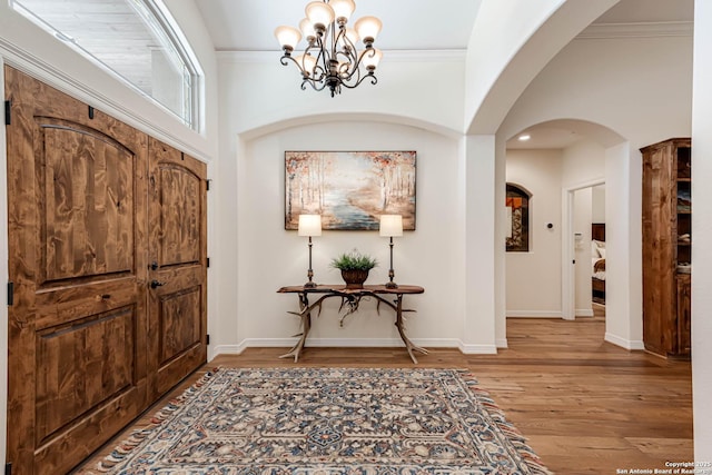 foyer with crown molding, baseboards, a notable chandelier, and wood finished floors