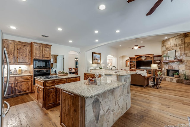 kitchen featuring a large island, arched walkways, a ceiling fan, black microwave, and light wood finished floors