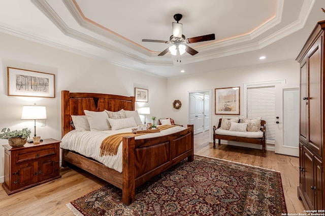 bedroom featuring light wood finished floors, ornamental molding, a ceiling fan, and a raised ceiling