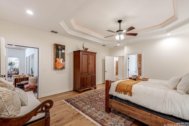 bedroom with ornamental molding, light wood-type flooring, a raised ceiling, and visible vents
