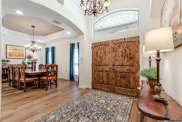 entryway featuring visible vents, a raised ceiling, arched walkways, an inviting chandelier, and light wood-style floors