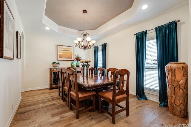 dining area featuring light wood-style flooring, baseboards, an inviting chandelier, and a raised ceiling