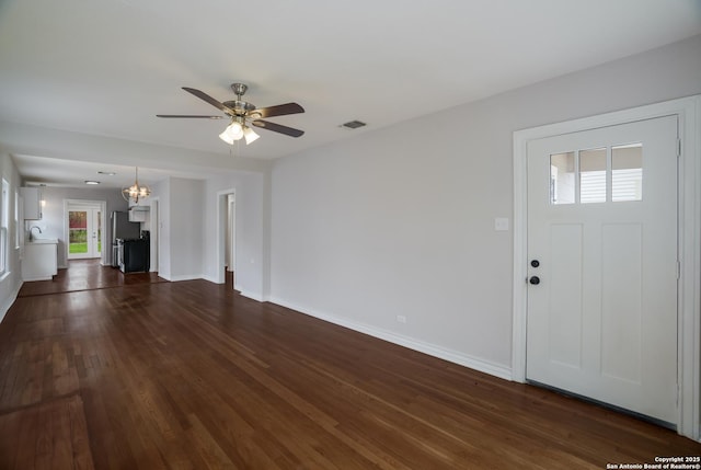 unfurnished living room with dark wood-type flooring, visible vents, baseboards, and ceiling fan with notable chandelier