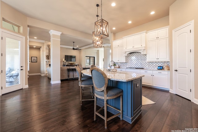 kitchen featuring dark wood-style flooring, backsplash, white cabinets, light stone countertops, and decorative columns