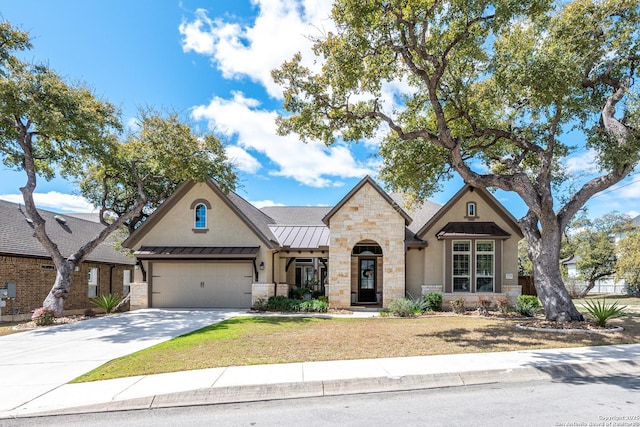 view of front facade with stucco siding, driveway, stone siding, a standing seam roof, and metal roof