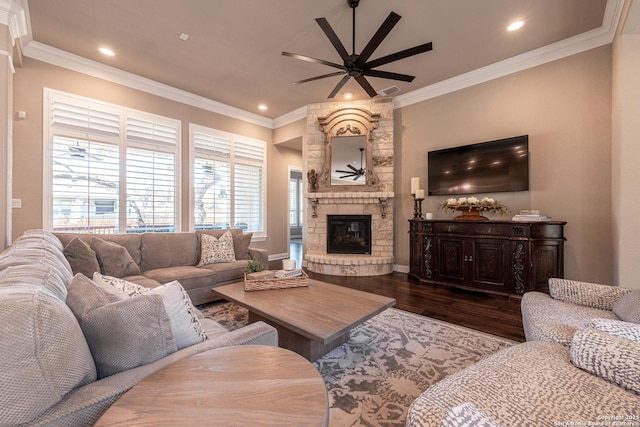 living area featuring dark wood-style floors, a stone fireplace, a ceiling fan, and crown molding