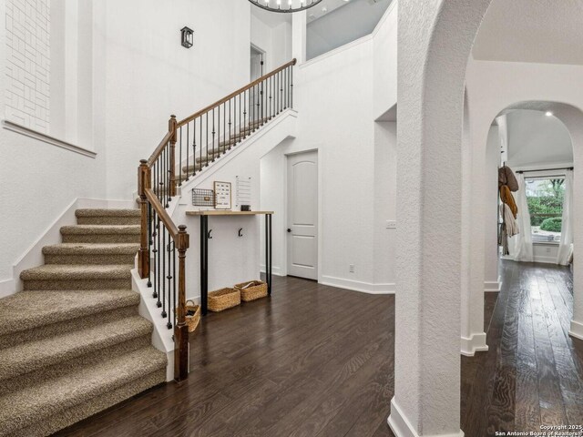 stairs with baseboards, arched walkways, a towering ceiling, and wood finished floors