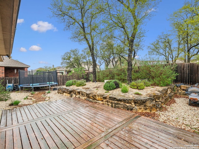 wooden deck with a trampoline and a fenced backyard