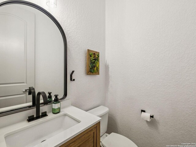 half bathroom with toilet, a textured wall, and vanity