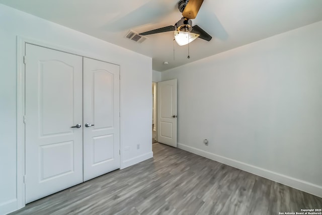 unfurnished bedroom featuring a closet, baseboards, visible vents, ceiling fan, and wood finished floors
