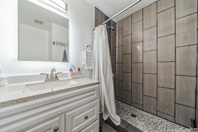 bathroom with tiled shower, a textured wall, and visible vents