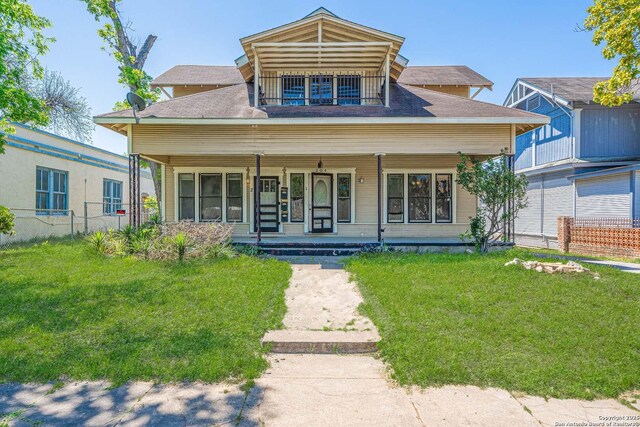 bungalow-style home featuring a front yard, a balcony, fence, and covered porch