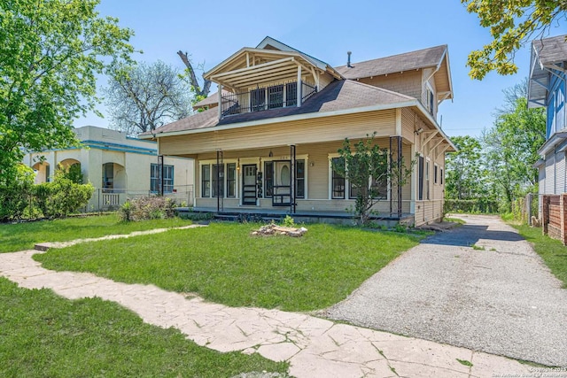 view of front of house featuring a porch, fence, a balcony, a front lawn, and driveway