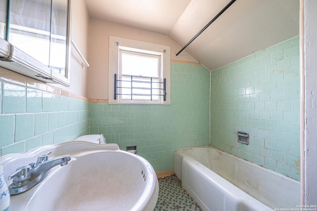 bathroom with a bath, a sink, tile walls, tile patterned floors, and lofted ceiling
