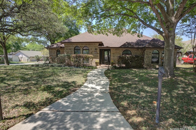 view of front of property with roof with shingles, a front yard, and brick siding