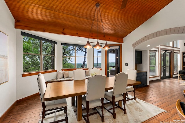 dining space featuring hardwood / wood-style flooring, arched walkways, baseboards, and vaulted ceiling