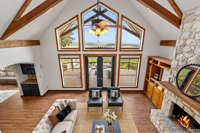 living area featuring high vaulted ceiling, a stone fireplace, beamed ceiling, baseboards, and dark wood-style flooring